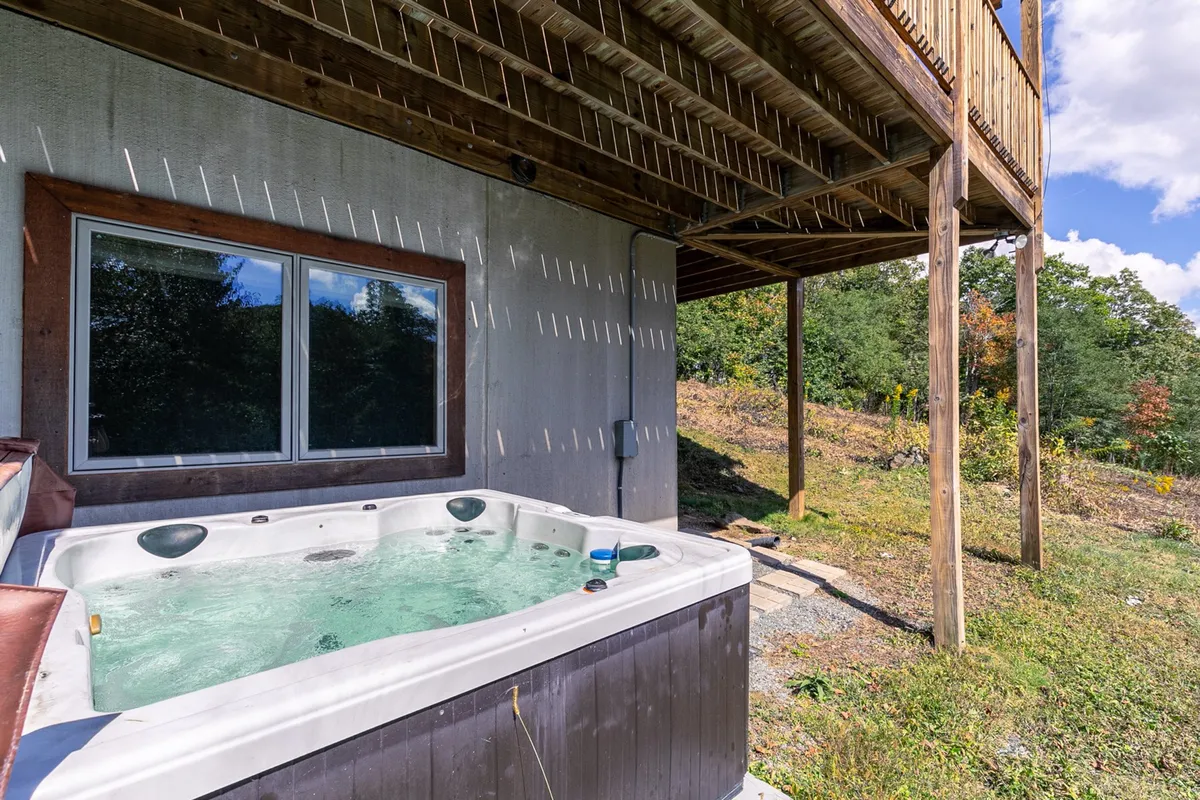 This image captures the inviting outdoor hot tub set against a backdrop of wooden pillars and the natural mountain landscape. The serene atmosphere features soft sunset lighting and hints of expansive views, emphasizing the relaxation awaiting after outdoor adventures.