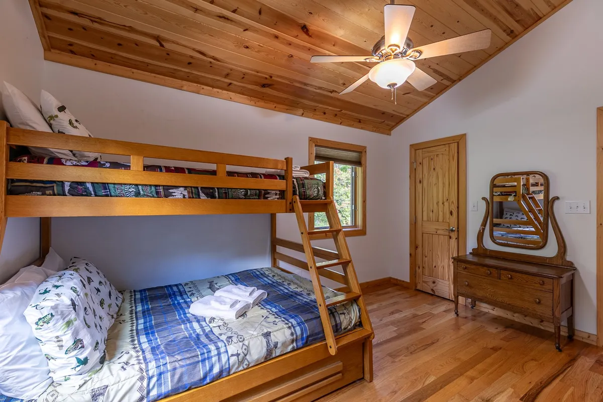 A bright, inviting bunk room with a twin-over-full bunk bed, wooden dresser, and a window that fills the space with natural light. The setup is perfect for kids or extra guests, offering both fun and practicality.