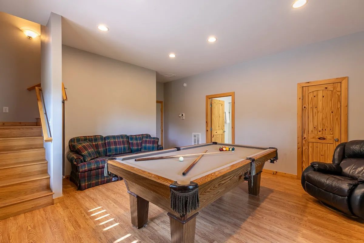 A casual, social space with a pool table as the centerpiece, a comfortable couch for spectators, and a staircase leading to other parts of the cabin. The setup encourages group interaction and leisure.
