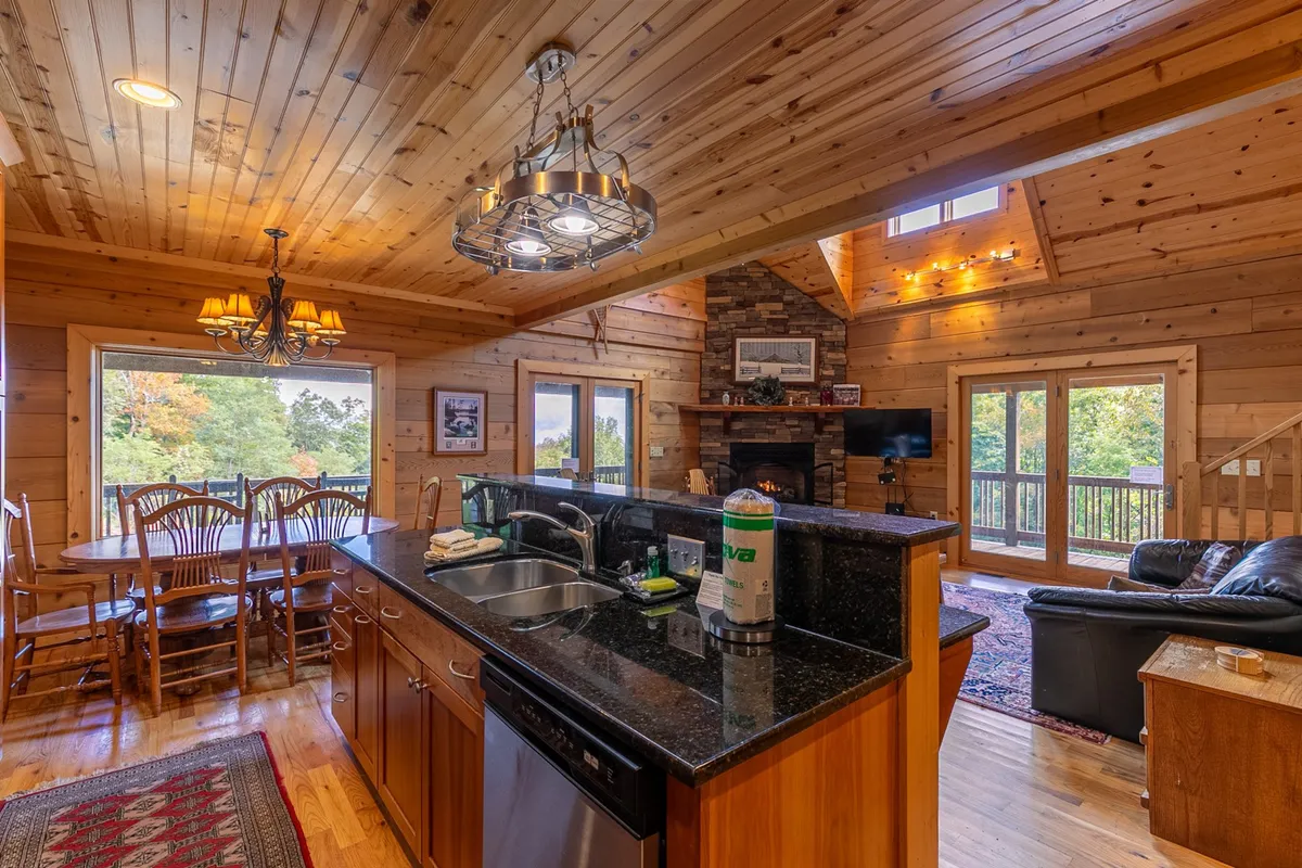 A broad view of the kitchen and dining area, featuring a kitchen island, dining table, and large windows that offer glimpses of the mountain scenery. The fireplace in the background adds warmth, while the overall design exudes comfort and spaciousness for both cooking and dining.