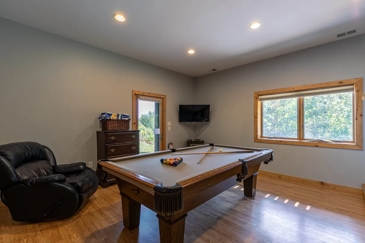 An airy entertainment loft featuring a pool table, leather chair, large window, and a wall-mounted TV. The space is bright and inviting, designed for friendly games and relaxed movie nights.