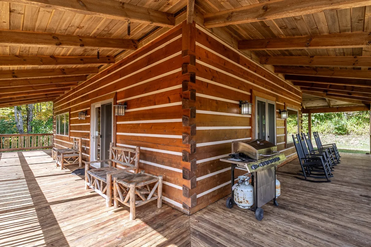 This image highlights the wooden cabin exterior with a gas grill, rocking chairs, and a welcoming outdoor seating area. The setting conveys a sense of family gatherings, alfresco dining, and tranquil mornings spent enjoying fresh air and vistas.